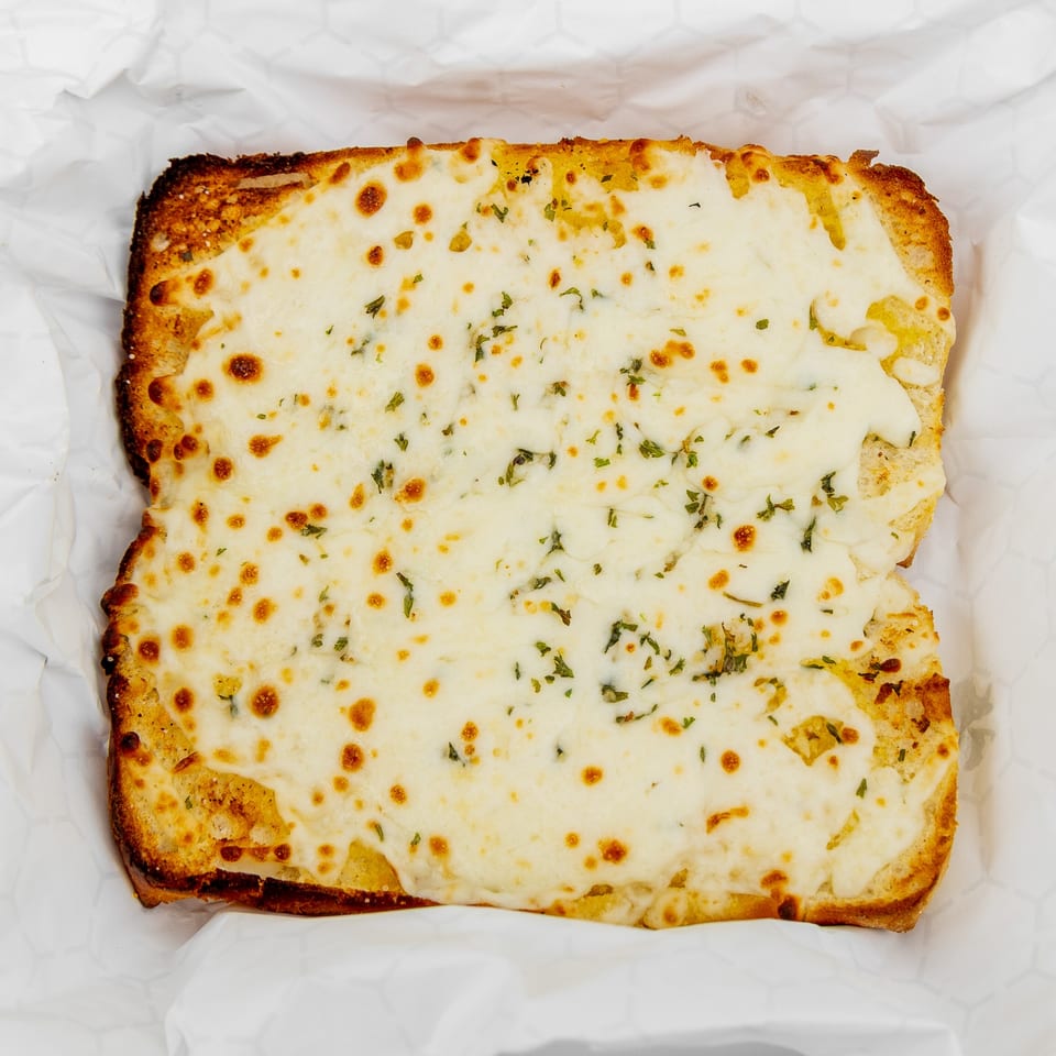 Cheesy garlic bread with melted mozzarella and green herbs, served in white paper.