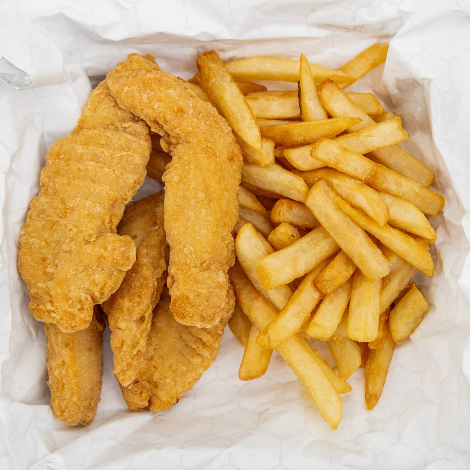 Golden-brown chicken tenders and thick-cut french fries in a white paper-lined basket.