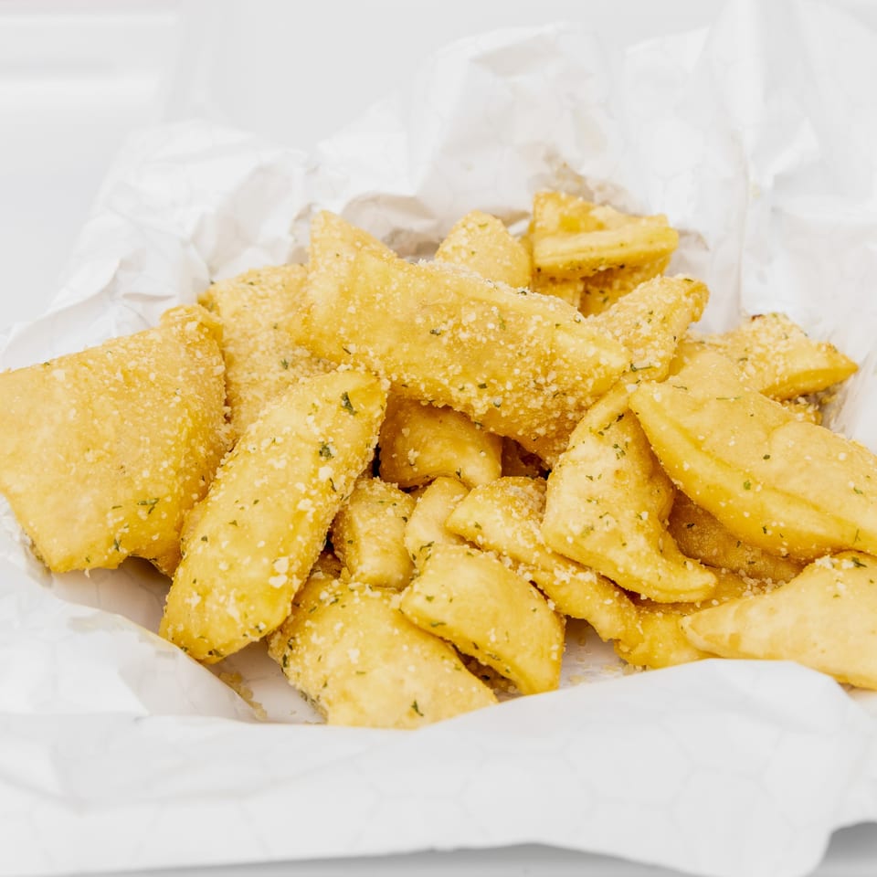 Golden fried dough knots, sprinkled with Parmesan cheese and herbs, in a white paper-lined basket.