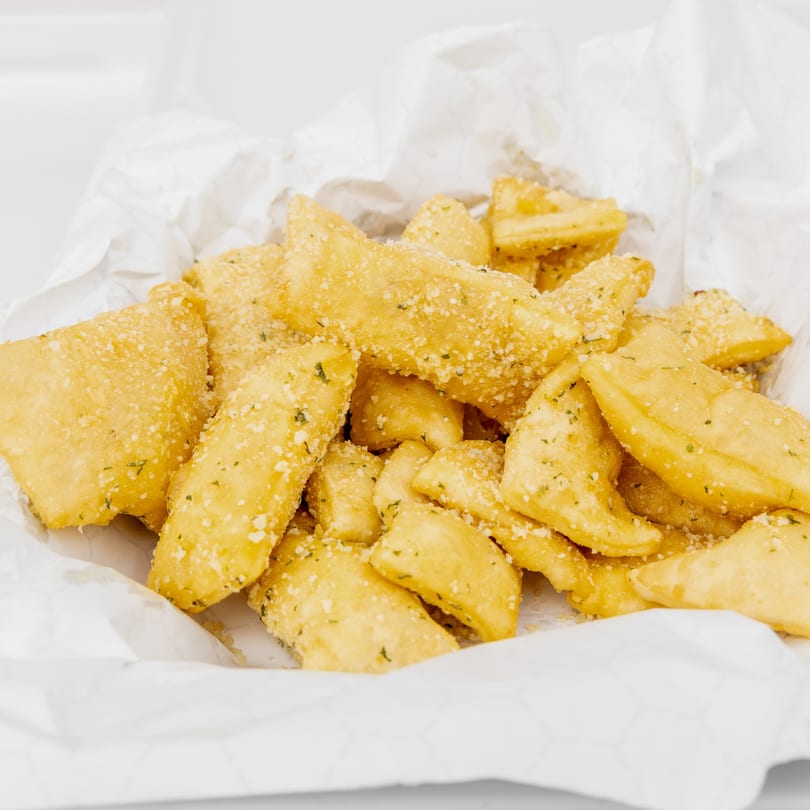 Golden fried dough knots, sprinkled with Parmesan cheese and herbs, in a white paper-lined basket.